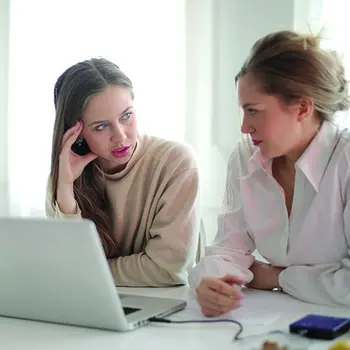Two people sitting in front of a laptop talking.