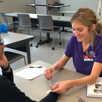 OTA student with a patient at a table