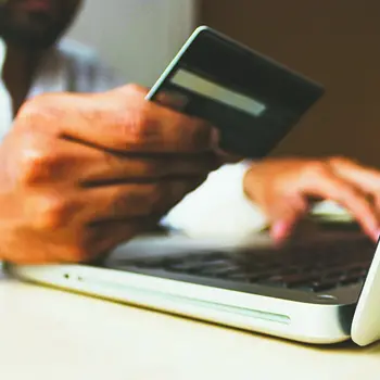 Persons hands. One typing on a laptop while the other hand holds a credit card.