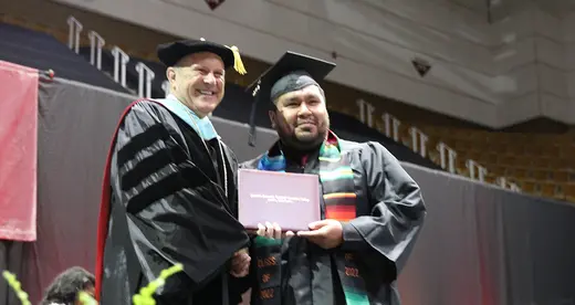 Dr. Gossett handing a diploma to male student at commencement