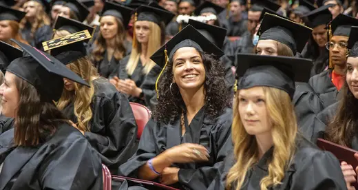 Student smiling while seated in her cap and gown at graduation