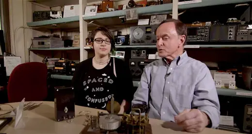 woman and man sitting at a table with an old radio in front of them