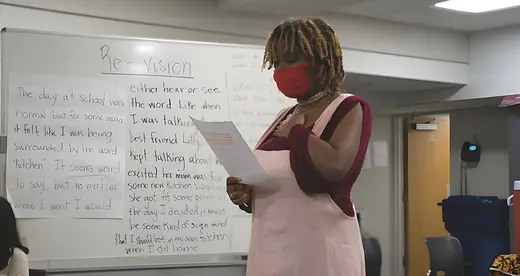 Young woman in mask standing reading a paper in a classroom
