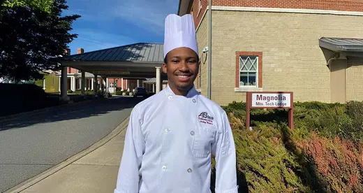 Young man in chef's uniform standing outside a building
