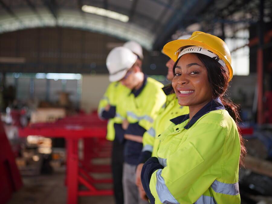 Black woman smiling, people in background, factory warehouse setting