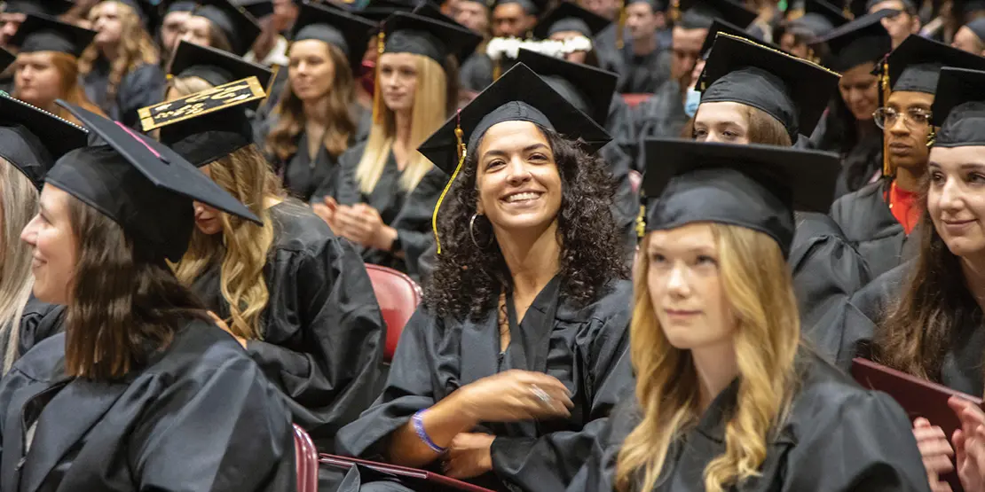 Student smiling while seated in her cap and gown at graduation