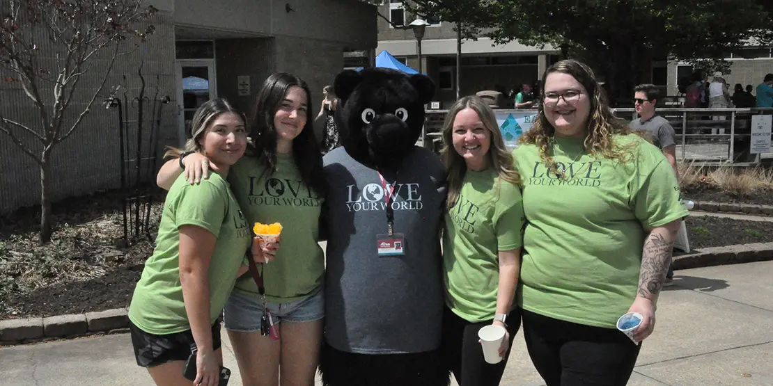 2 A-B Tech students posing with the A-B Tech Trailblazer bear wearing lime green Earth Day t-shirts.