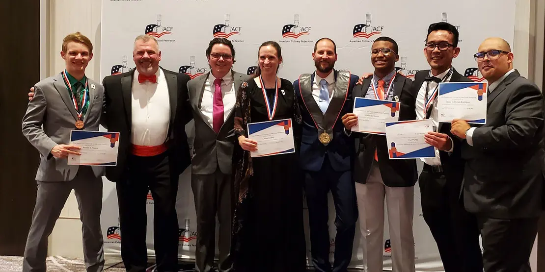 Eight people in formal wear standing in front of a wall with ACF logos