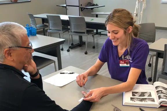 OTA student with a patient at a table